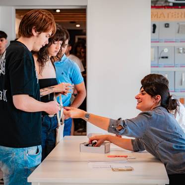 Un grupo de personas interactuando en un espacio moderno, donde una persona atiende a otra en una mesa.
