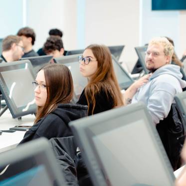 Un grupo de estudiantes sentados en un aula con computadoras frente a ellos.