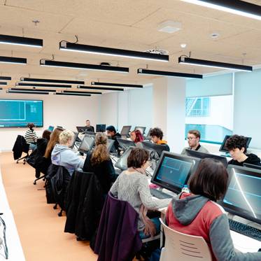 Un grupo de estudiantes trabaja en computadoras en un aula moderna.