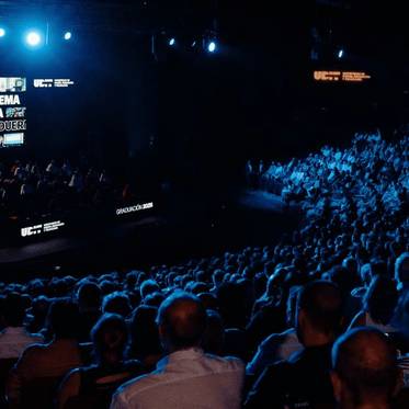 Una multitud asiste a una ceremonia de graduación iluminada por luces azules.