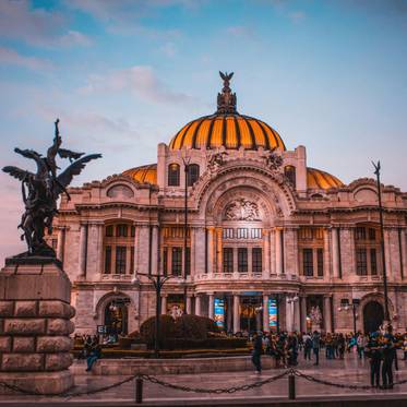 Edificio monumental con cúpula de color amarillo y una estatua en primer plano durante el atardecer.