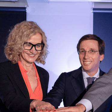 Dos personas sonríen mientras se tocan las manos en un entorno formal.