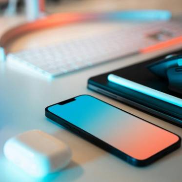 Una imagen que muestra un teléfono, auriculares, un ratón y una tablet sobre una mesa con iluminación tenue.