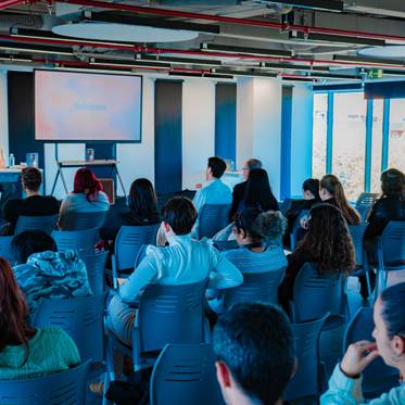 Una conferencia con un ponente frente a una audiencia sentada en un espacio moderno.