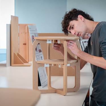 Un joven está ensamblando una estructura de madera en un entorno de trabajo.