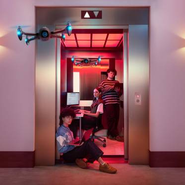 Un grupo de jóvenes interactúa con drones en un ascensor iluminado con luces de colores.