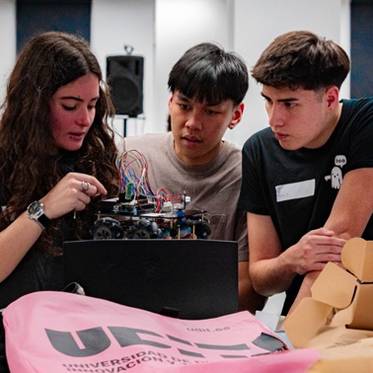Un grupo de tres jóvenes trabaja juntos en la construcción de un robot en un entorno educativo.