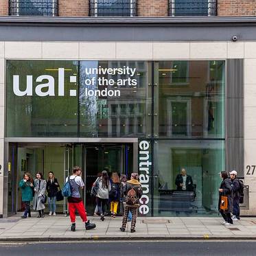 La imagen muestra la entrada de la Universidad de las Artes de Londres con varias personas entrando y saliendo.