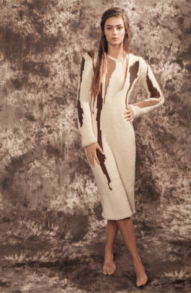 Una modelo posa con un vestido de punto en tonos claros y oscuros sobre un fondo texturizado.
