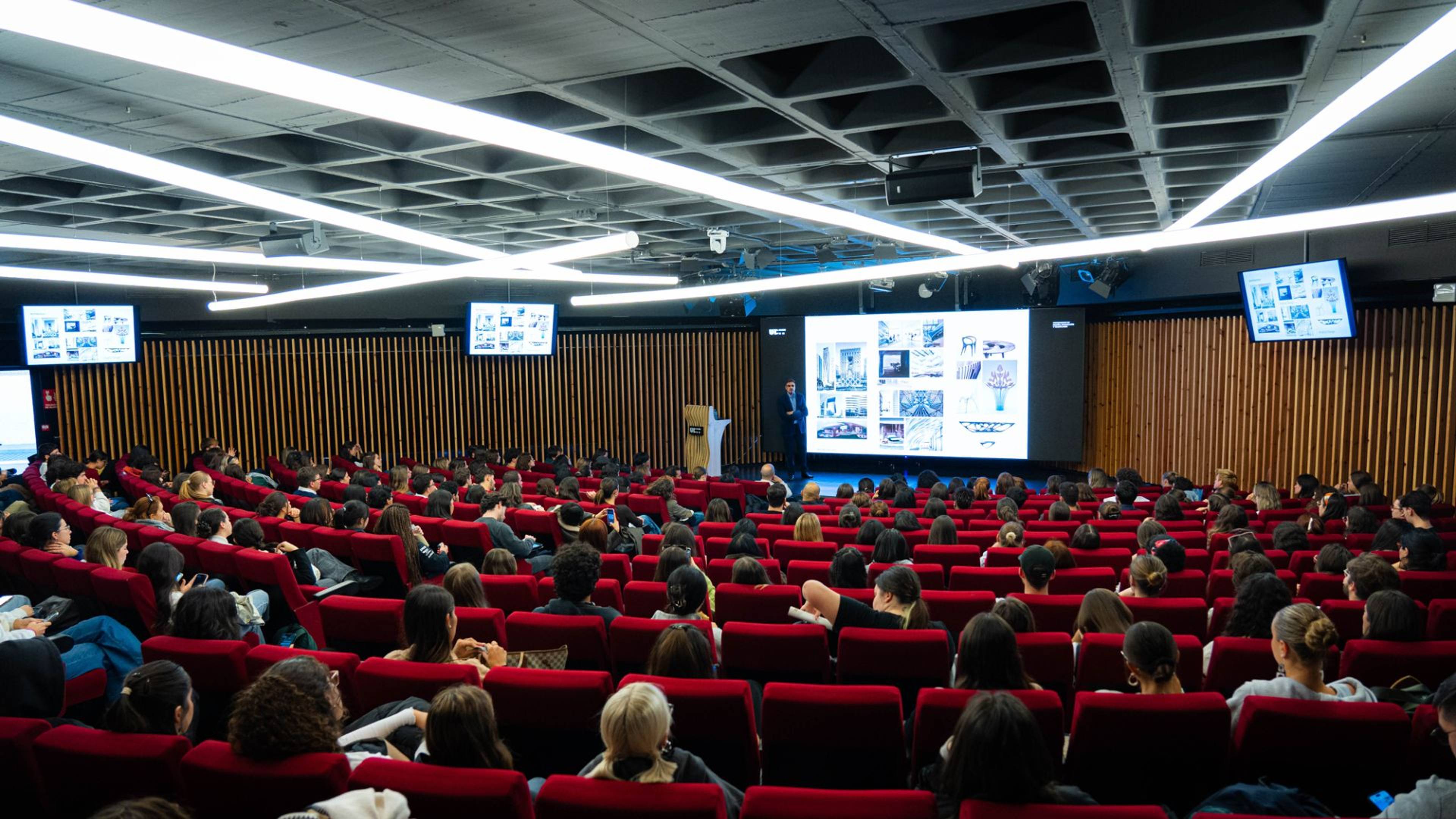 Una sala de conferencias llena de estudiantes atentos a una presentación en una pantalla grande.