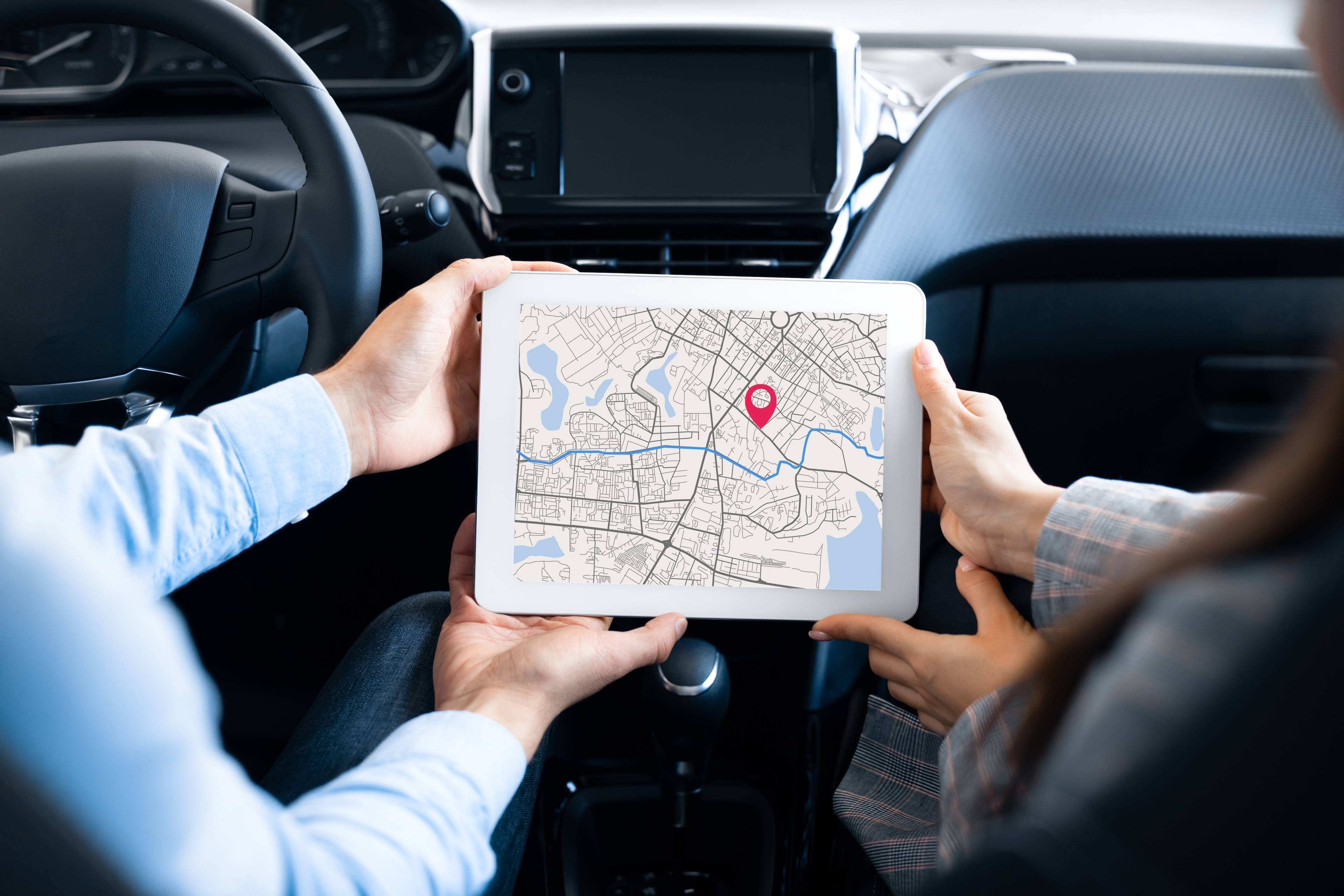 Una pareja en un coche mirando un mapa en una tablet.