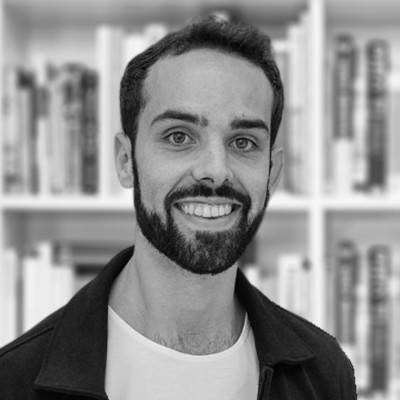 Una persona sonriente con barba y atuendo casual frente a estanterías de libros.