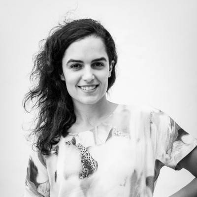 Una mujer sonriente con una camiseta de diseño colorido posa frente a un fondo blanco.