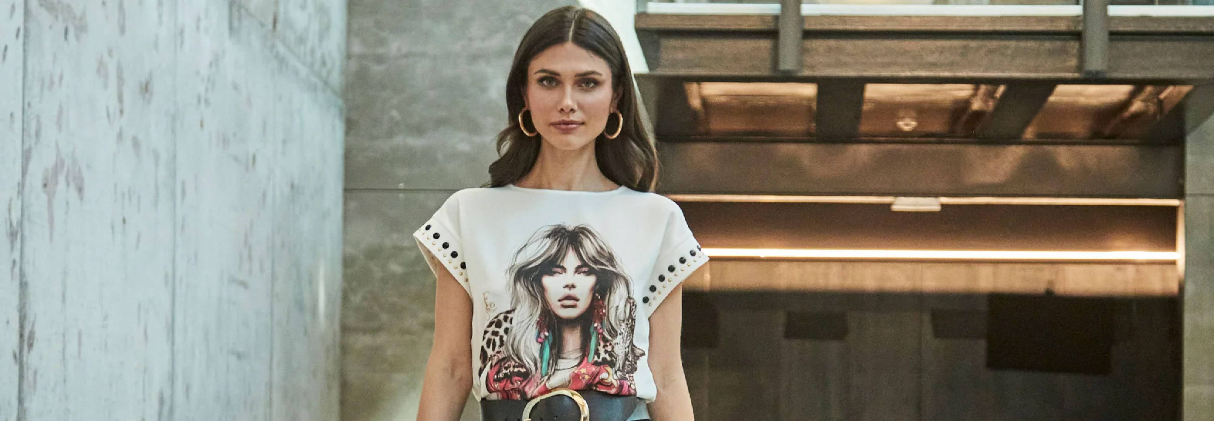 Una mujer camina por un pasillo moderno luciendo una camiseta con un diseño artístico.