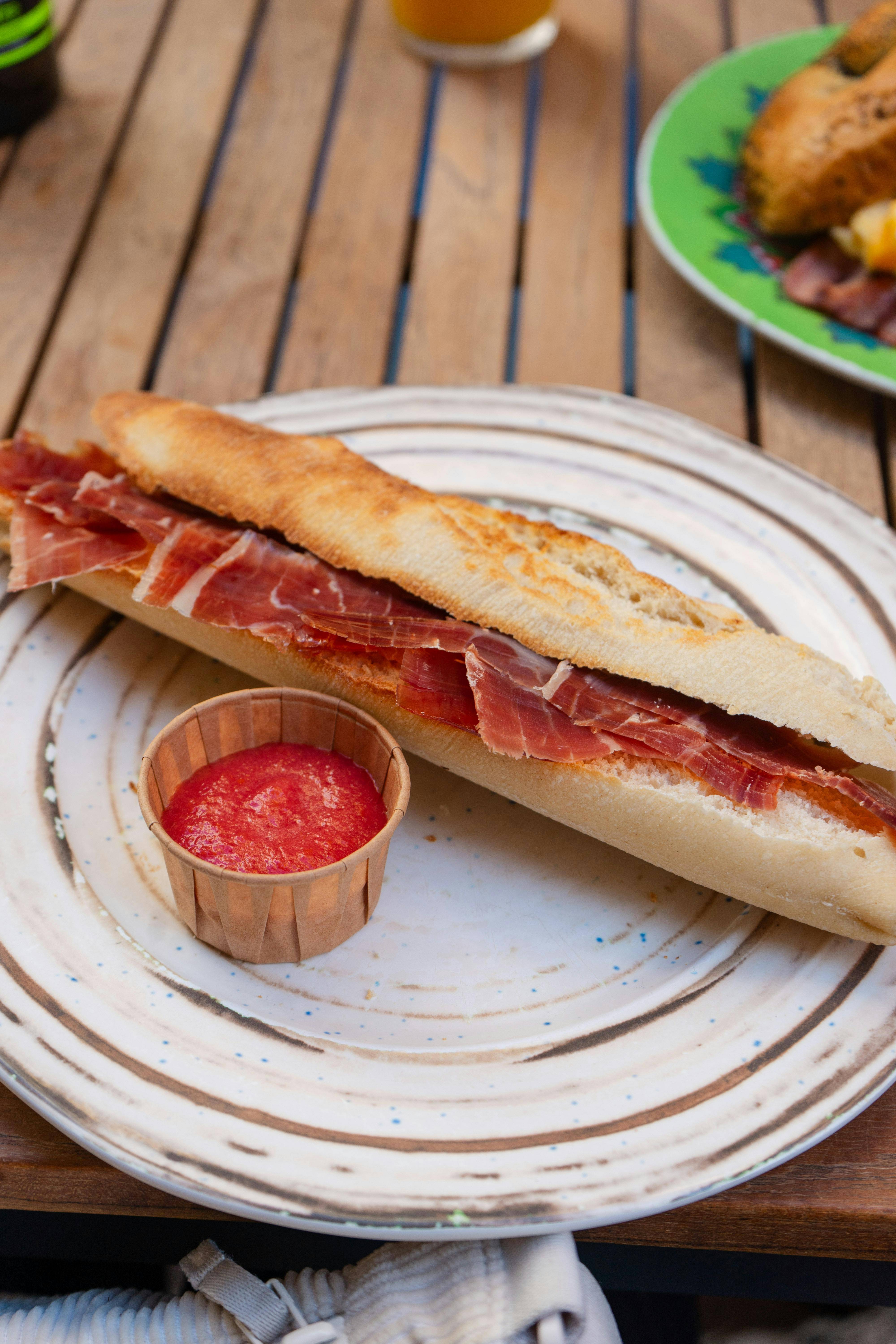 Un delicioso bocadillo de jamón servido en un plato con una salsa roja.