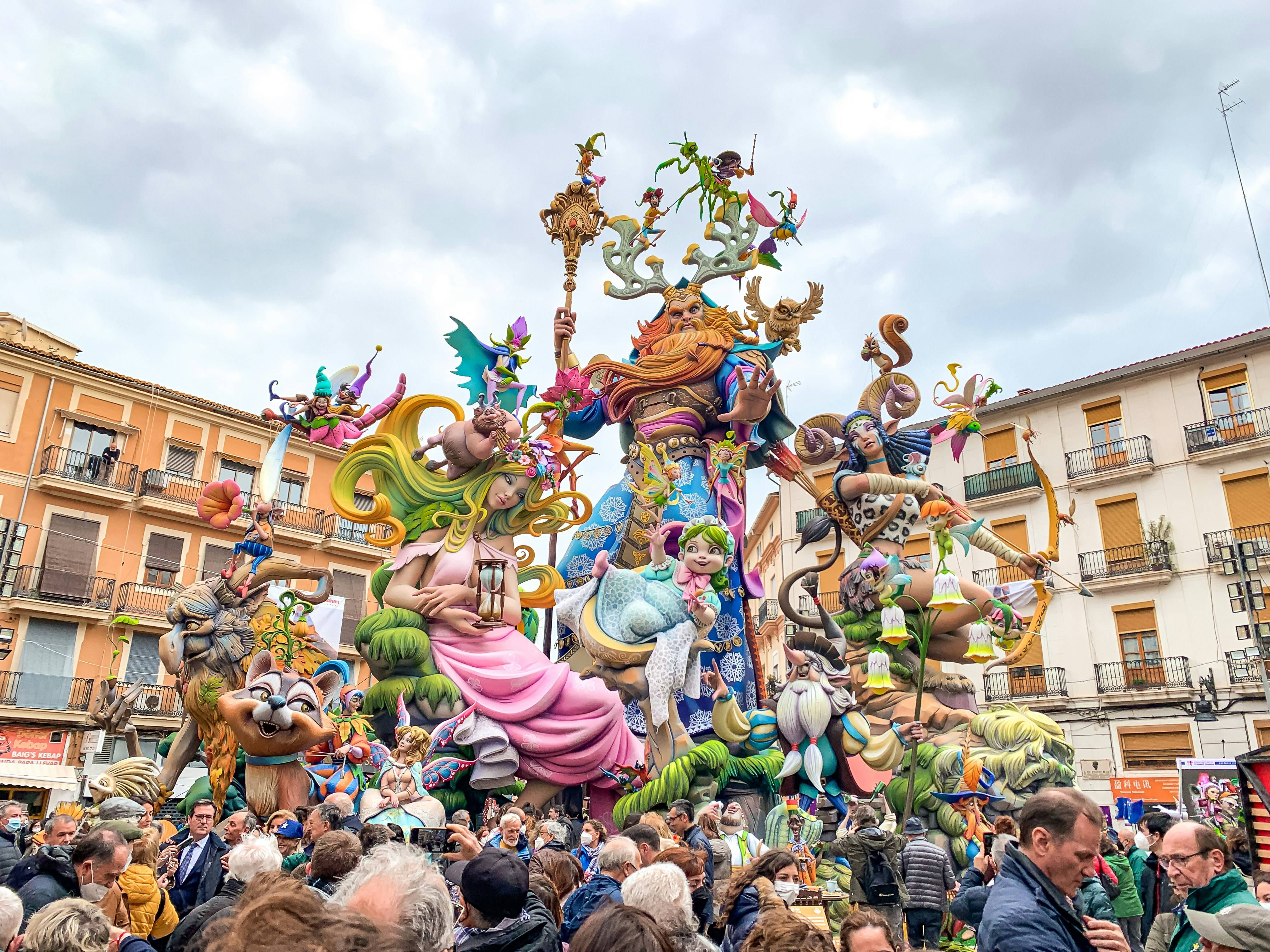 Una multitud se reúne alrededor de un impresionante monumento festivo decorado con figuras coloridas y elaboradas.