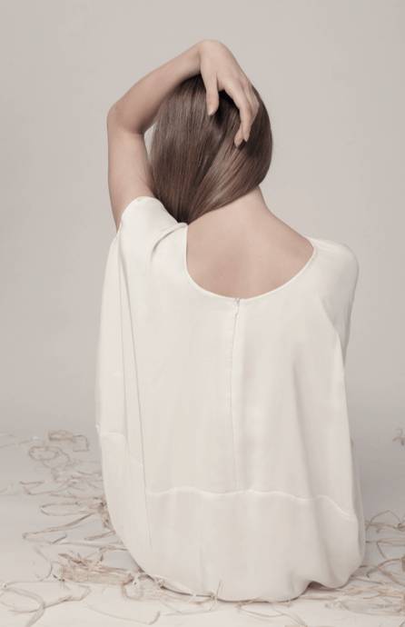 Una mujer con blusa blanca mirando hacia atrás y tocándose el cabello.