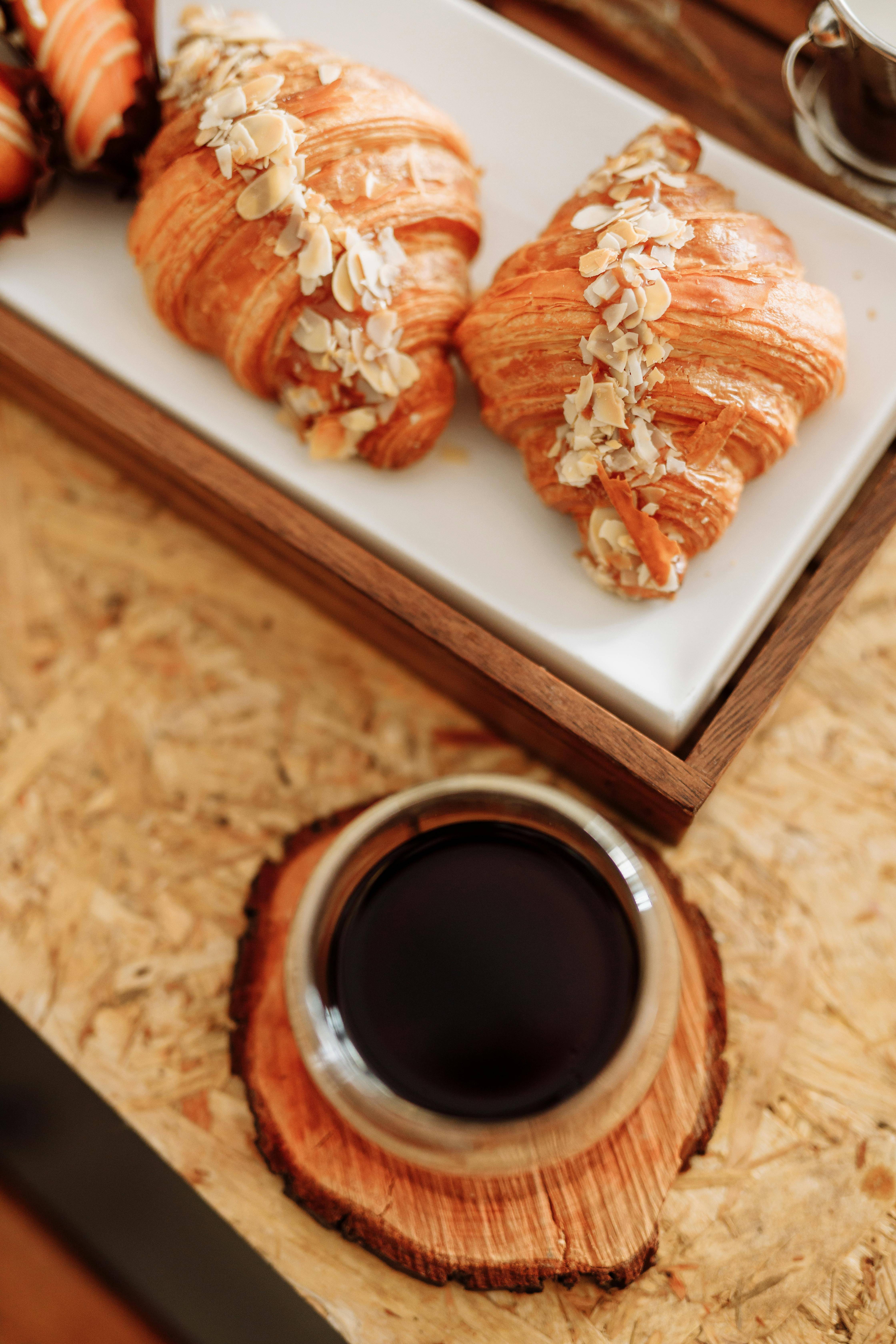 Dos croissants con almendras y una taza de café sobre una mesa de madera.