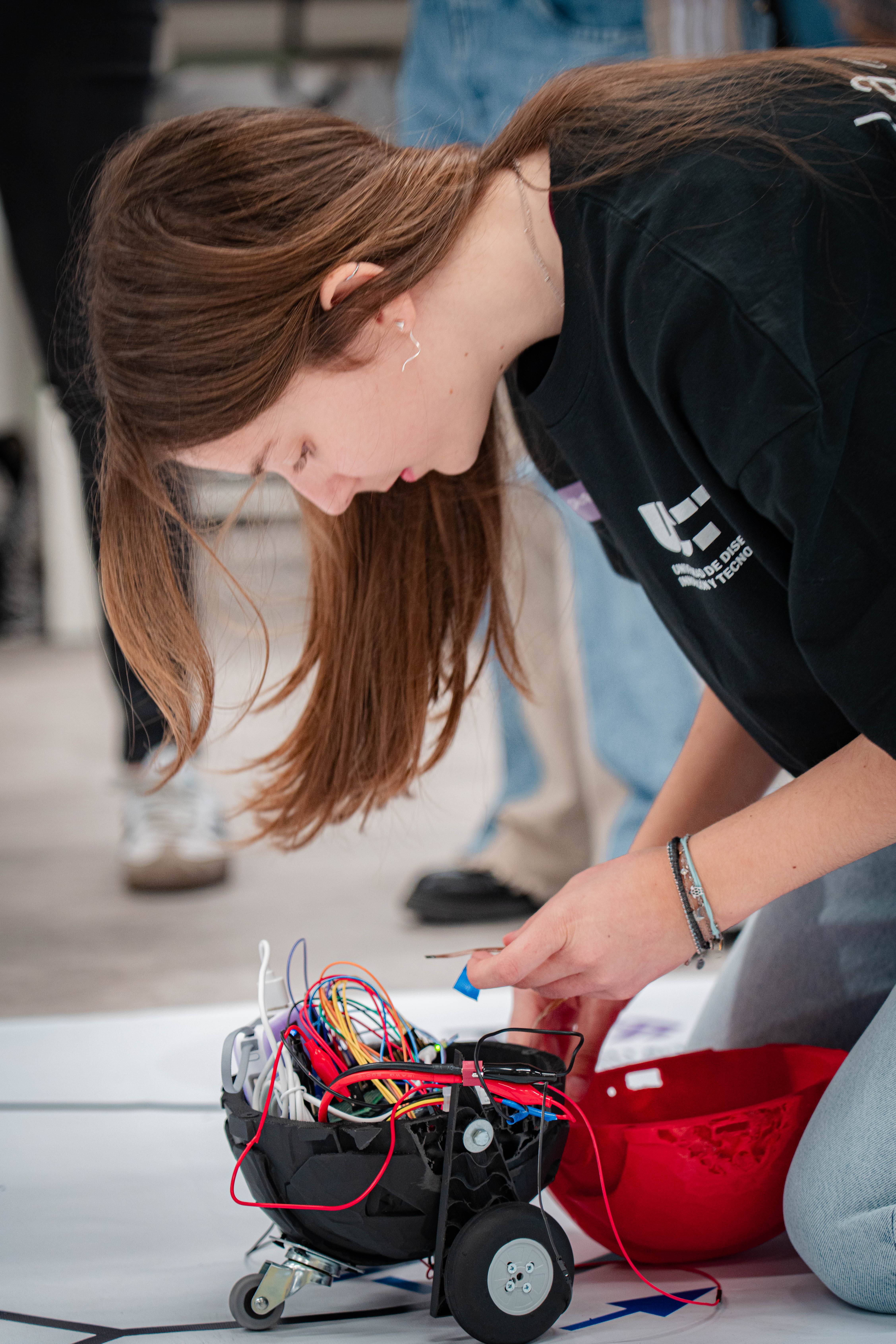 Una joven está trabajando en un robot con cables en un entorno de taller.