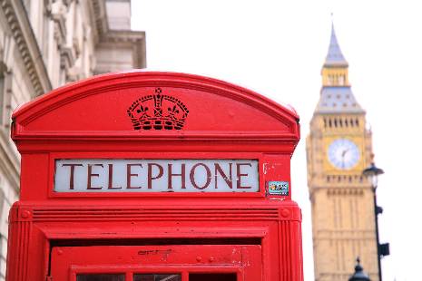Una cabina telefónica roja en primer plano con el reloj de Big Ben al fondo.