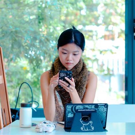 Una joven sentada en una mesa moderna, mirando su teléfono móvil con atención.