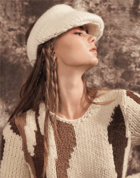 Una modelo con un suéter de lana de diseño abstracto y una visera blanca observa con una actitud elegante.