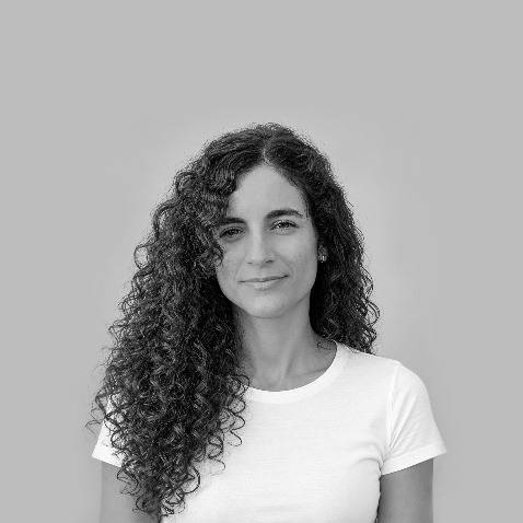 Una mujer con cabello rizado y oscuro, sonriendo frente a un fondo gris.