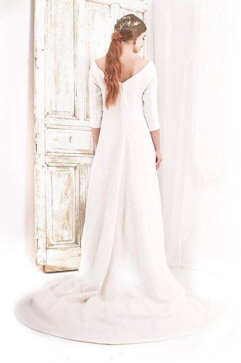 Una mujer con un vestido de novia blanco se encuentra de espaldas frente a una puerta antigua.