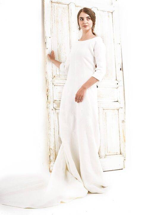 Una mujer luce un vestido blanco elegante junto a una puerta antigua.
