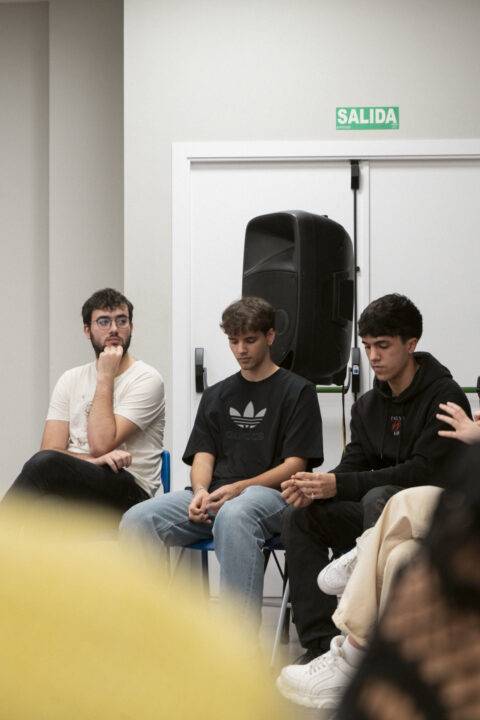 Tres jóvenes sentados en sillas durante una conversación en un ambiente interior.