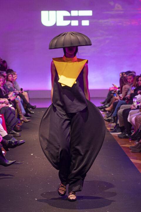 Una modelo camina por la pasarela luciendo un diseño de moda avant-garde con un sombrero en forma de paraguas.