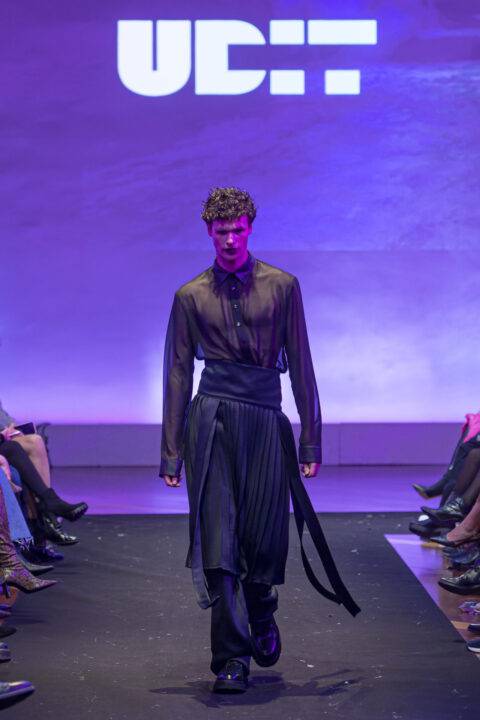 Un modelo masculino camina por la pasarela luciendo un atuendo elegante en un desfile de moda.