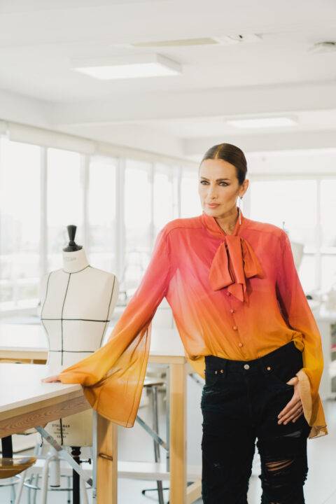 Una mujer posa con una blusa de colores vibrantes en un estudio de diseño.