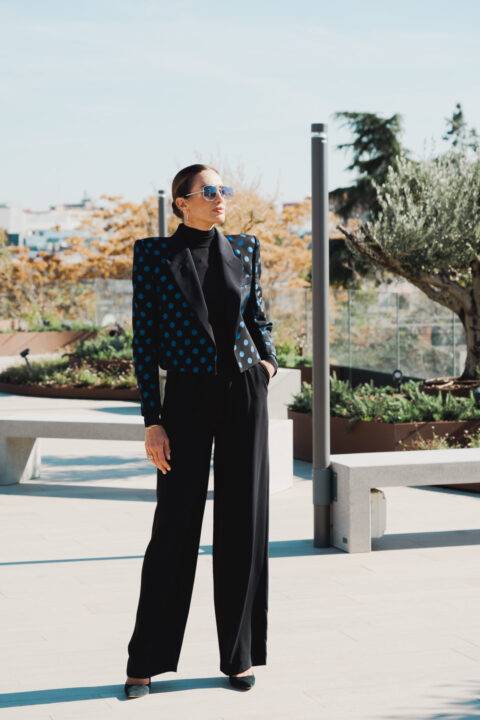 Una mujer elegante con un blazer de lunares y pantalones anchos, posando en un entorno urbano.