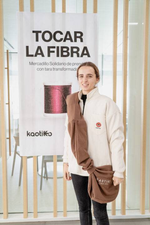 Una persona posa frente a un cartel que dice 'TOCAR LA FIBRA' en un mercadillo solidario.