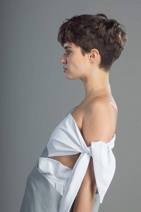Un retrato de perfil de una persona con cabello corto que lleva una blusa de color claro.