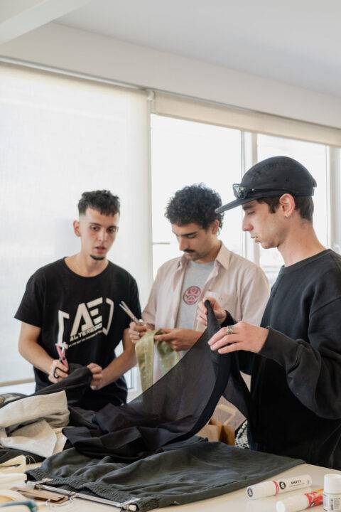 Tres jóvenes se encuentran en una mesa revisando ropa en un ambiente iluminado.