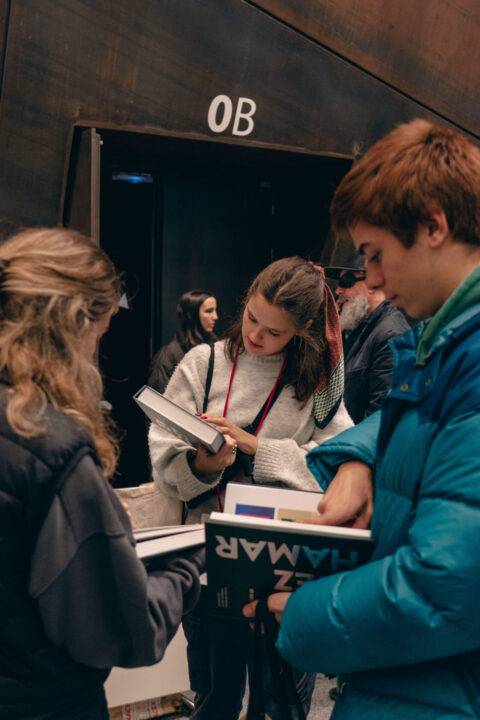 Un grupo de personas revisa libros dentro de un recinto con una puerta marcada con el número OB.