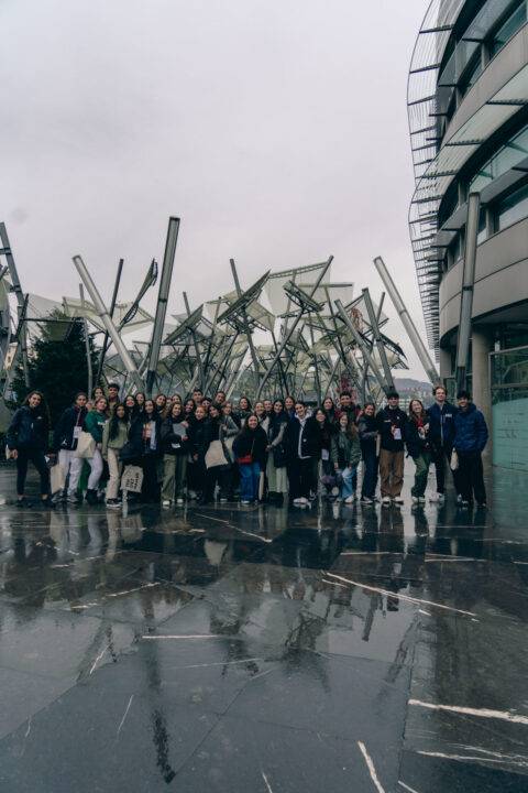 Un grupo grande de personas posando frente a una estructura moderna en un día nublado.