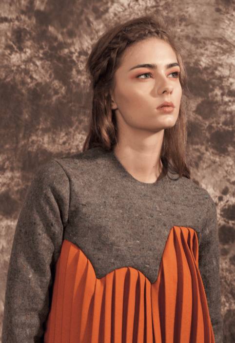 Una modelo posando con un vestido de colores gris y naranja en un fondo texturizado.