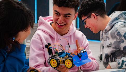 Un grupo de jóvenes se divierten mientras trabajan en un robot móvil que han construido juntos.
