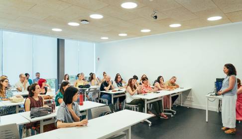 Una sala de clases con numerosos estudiantes atentos a una presentación.