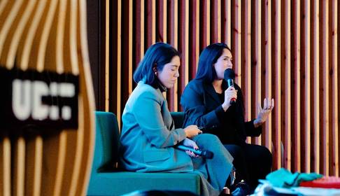 Dos mujeres participan en una conversación en un evento, una de ellas habla mientras la otra escucha.