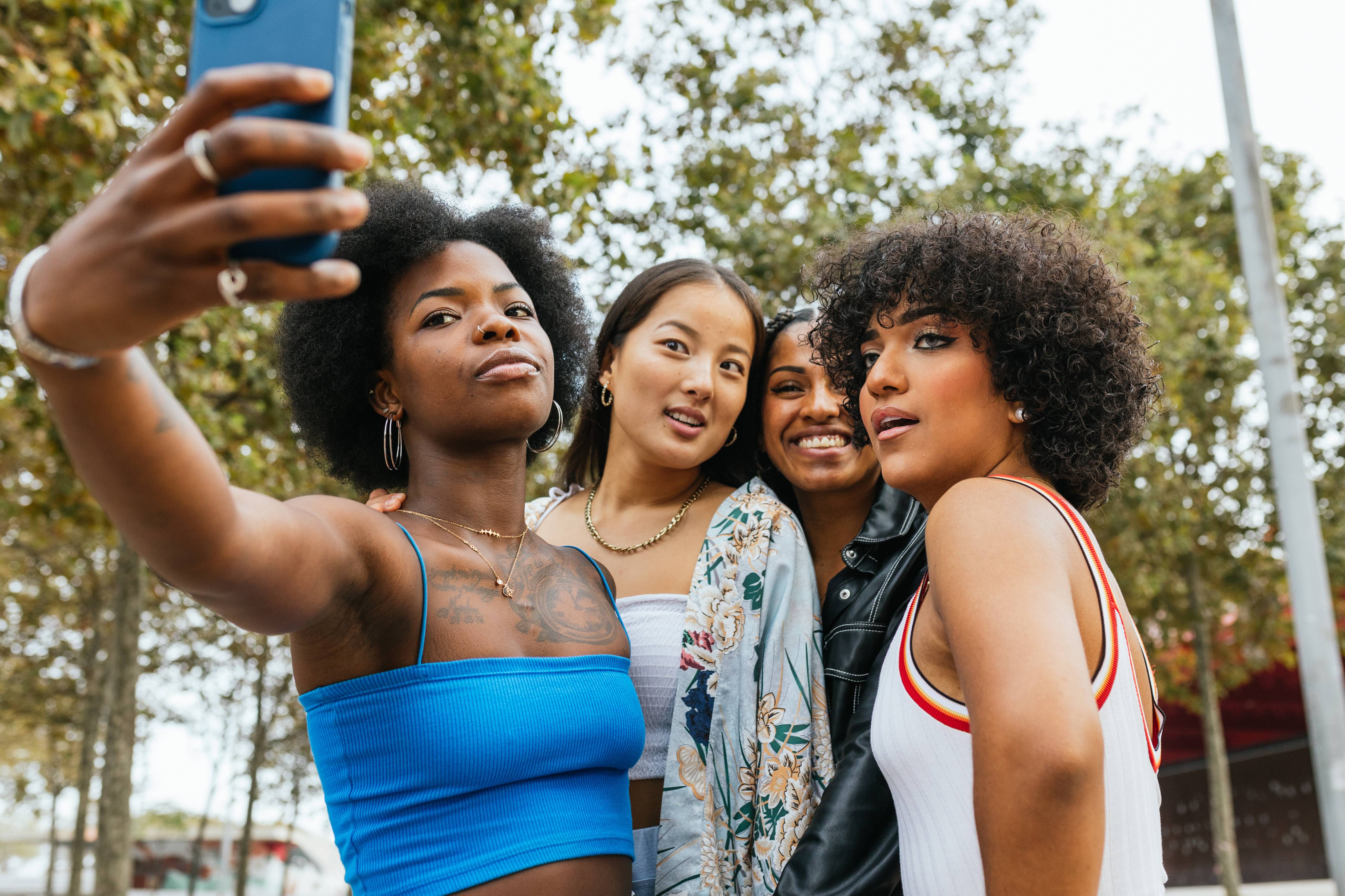 Cuatro amigas posando juntas y tomando una selfie al aire libre.