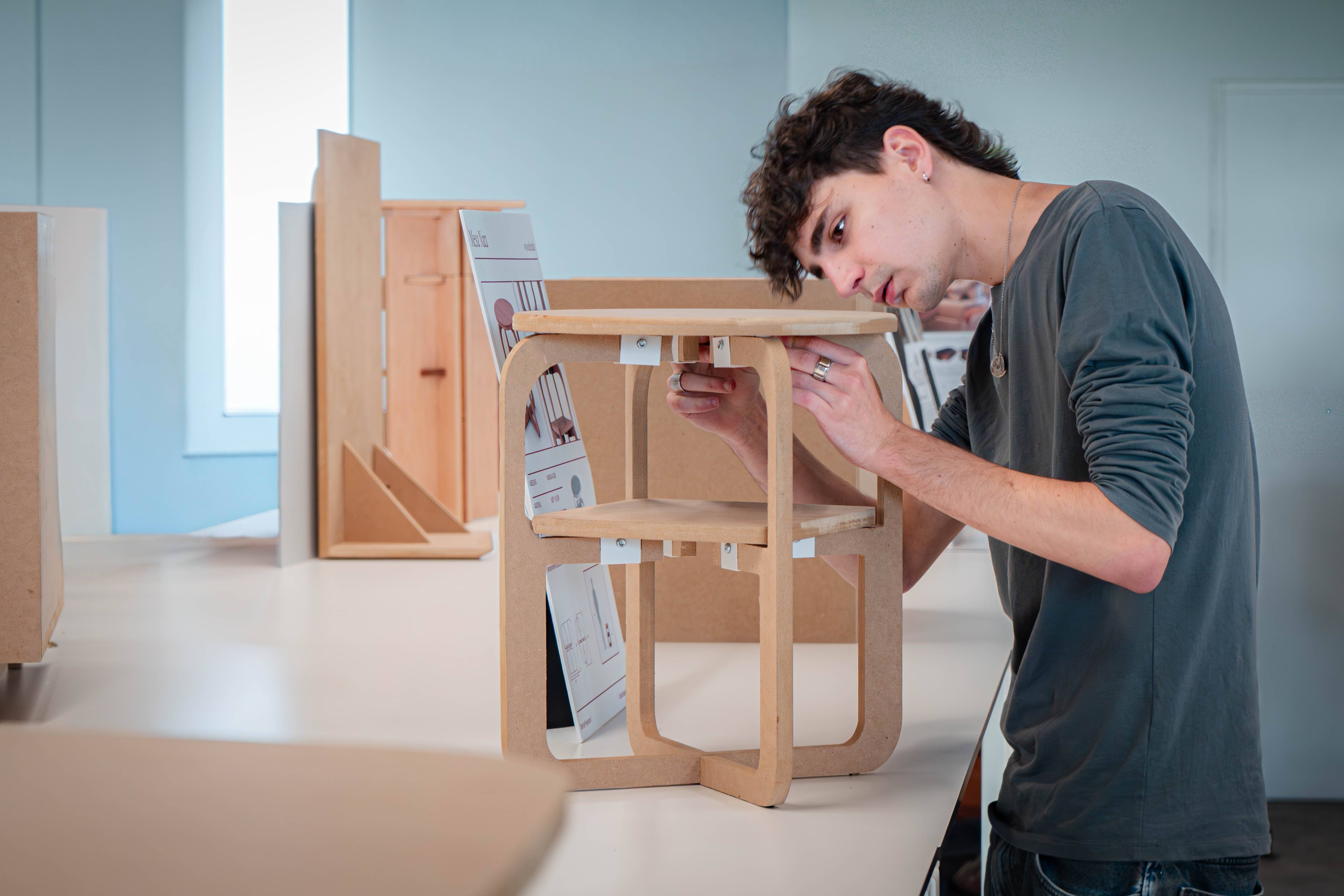Un joven está ensamblando un mueble de madera en un entorno de trabajo moderno.