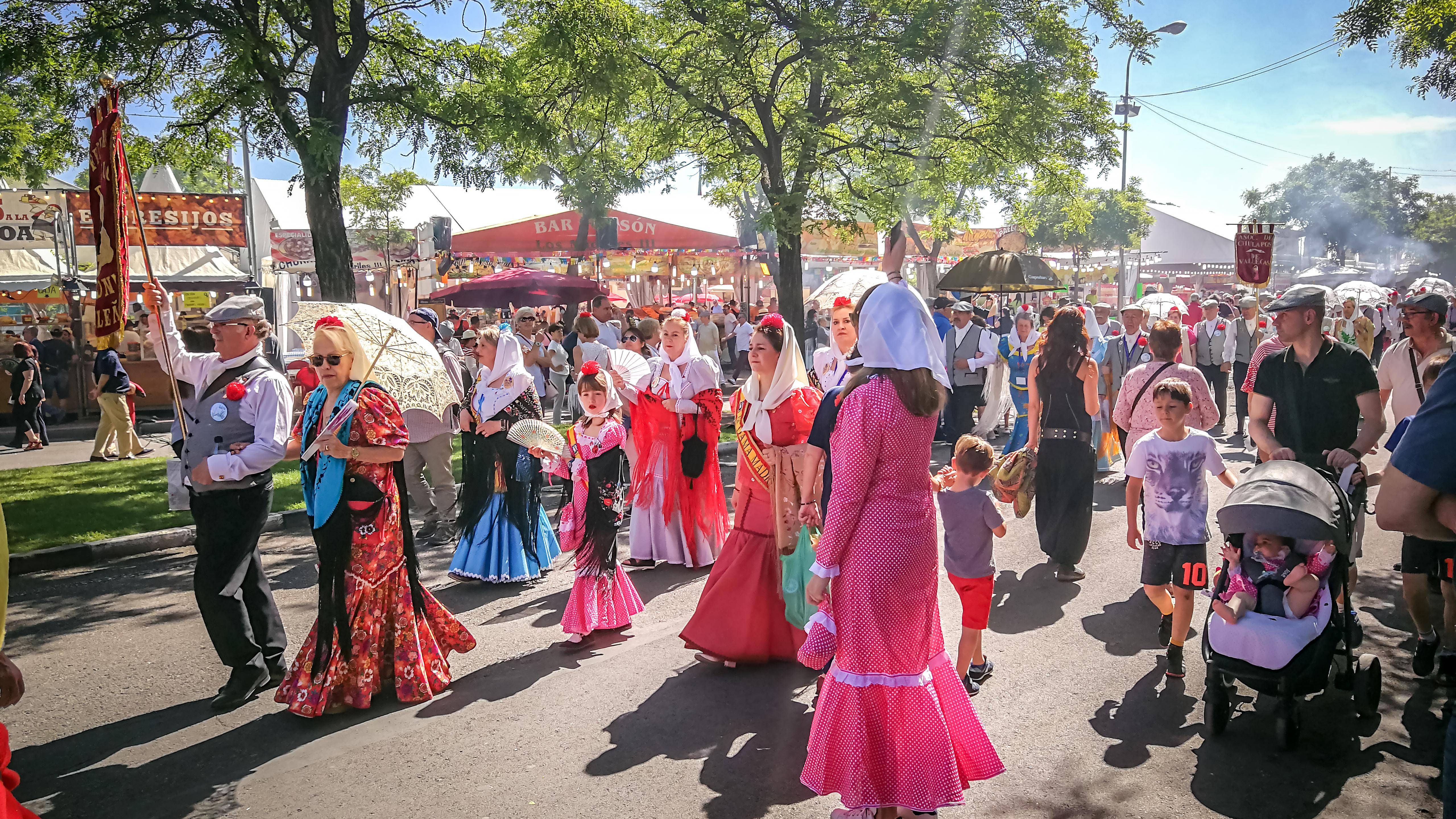 Una multitud de personas vestidas con trajes tradicionales caminan por una feria al aire libre.