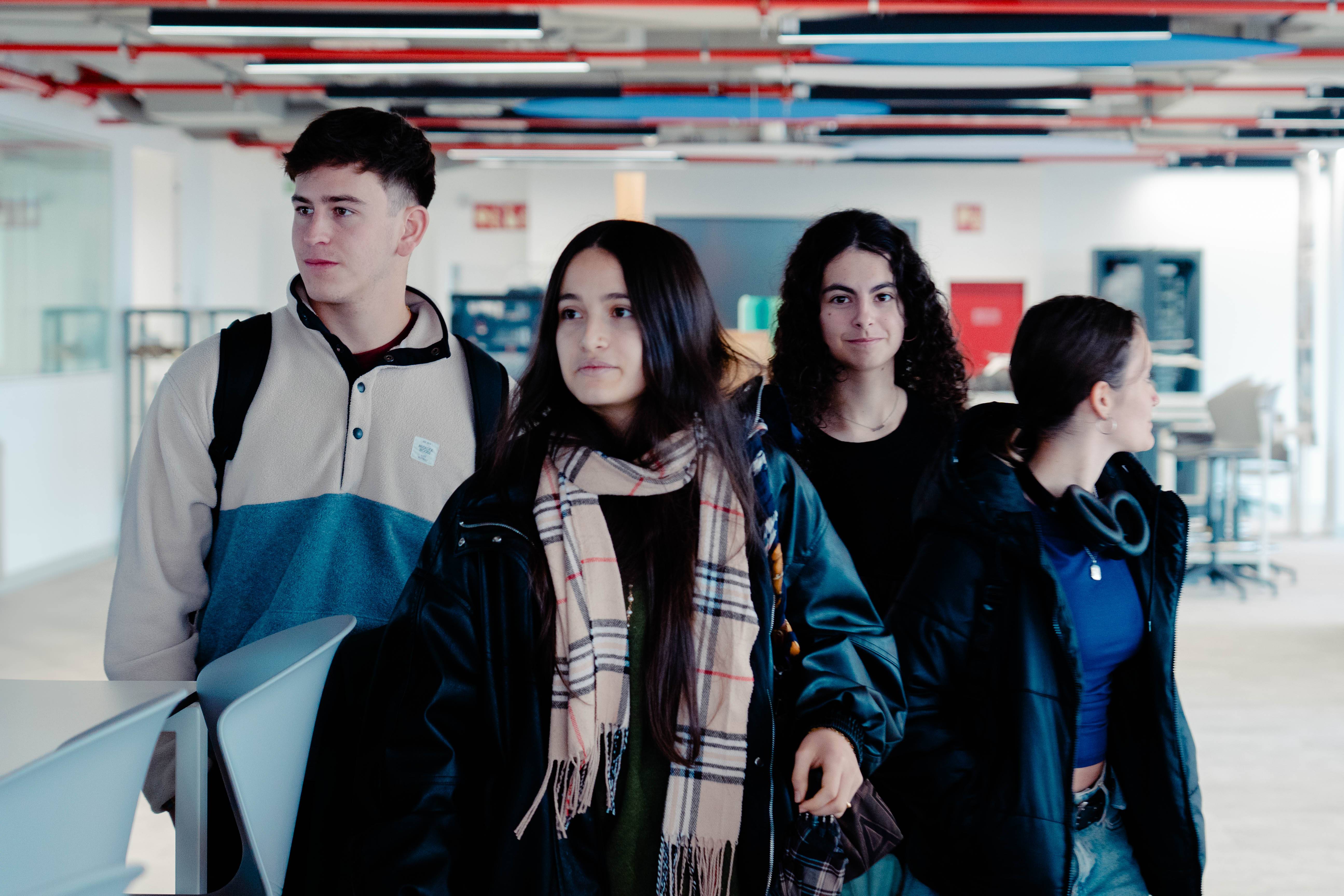 Un grupo de cuatro jóvenes camina juntos por un espacio interior moderno.