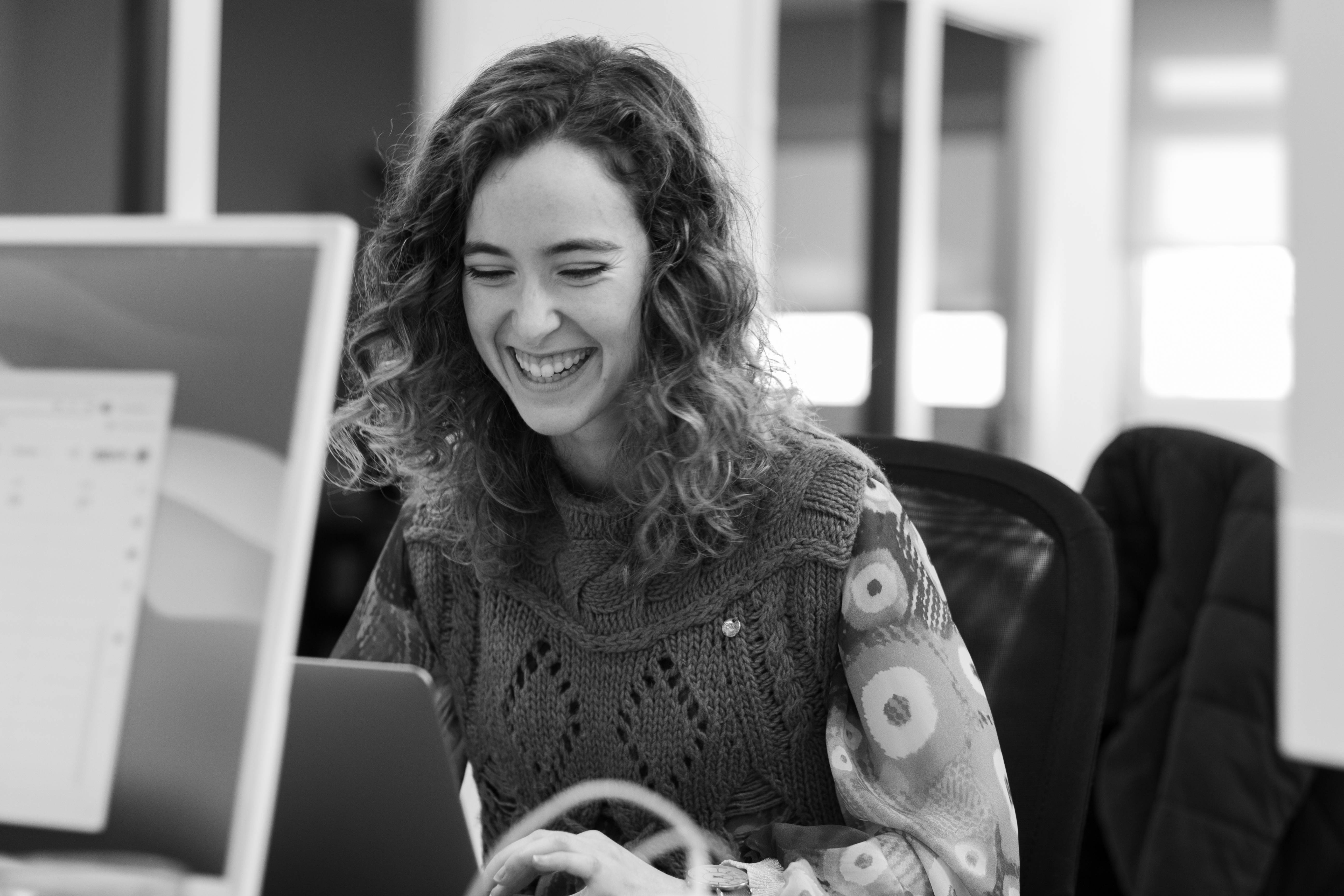 Una mujer sonriente trabaja en su computadora portátil mientras se encuentra en un entorno de oficina.