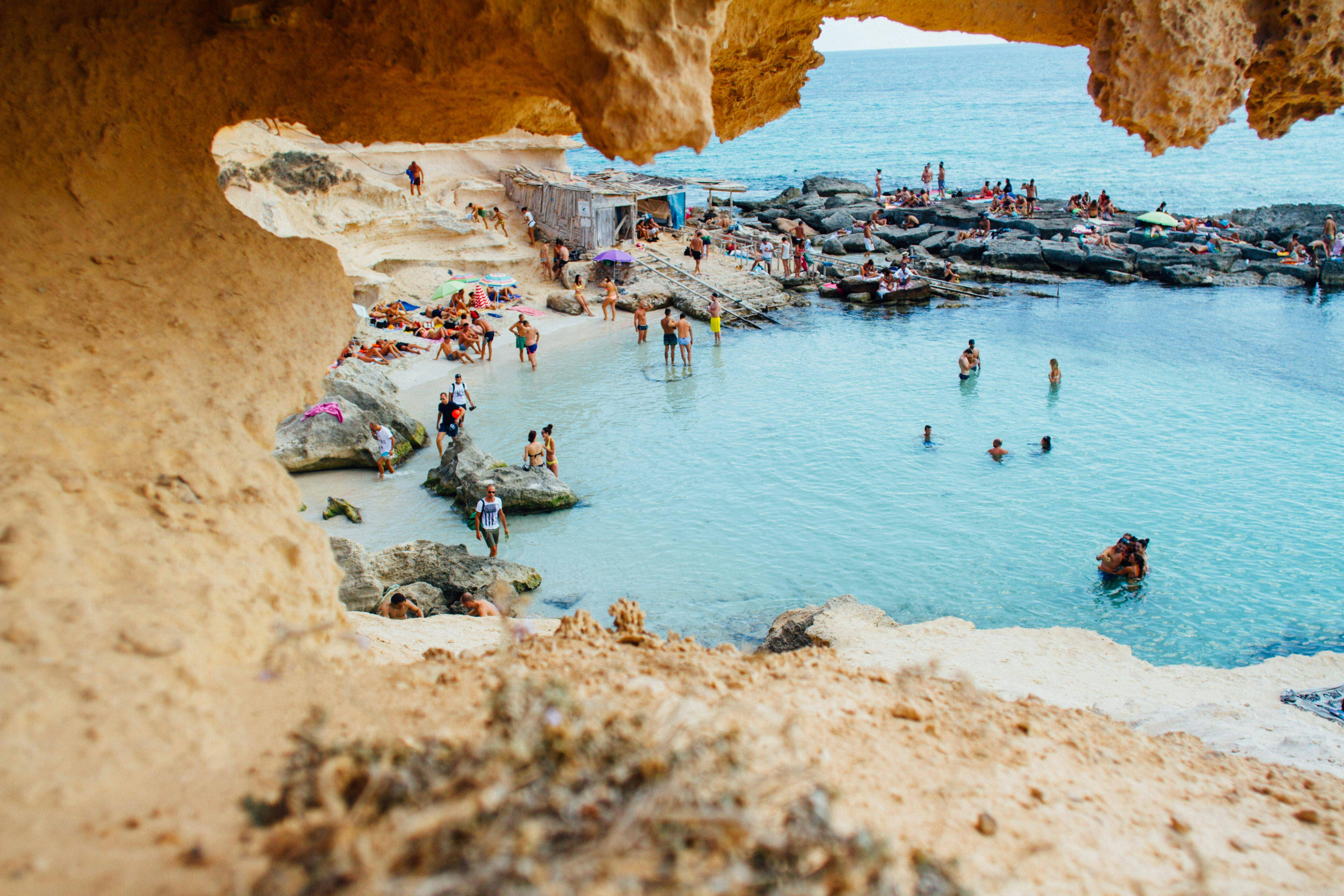 Una playa con gente disfrutando del sol y el agua en un entorno rocoso.