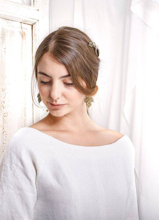 Una joven con peinado casual y blusa blanca se encuentra en un ambiente iluminado y sencillo.